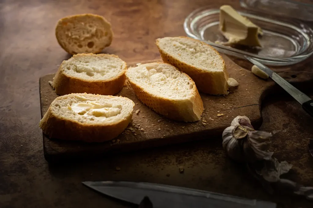 Fotografia kulinarna: kromki pieczywa na drewnianej desce, masło i nóż w kuchennym klimacie